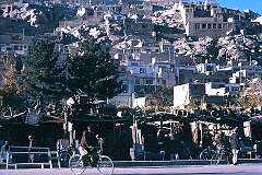 A corner of Kabul with houses on the hill and shops along the street.