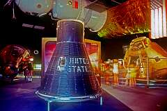 A Gemini space capsule with overhead a model of the Soviet Soyuz capsule and in the background an Apollo cabin; at the Kennedy Space Center Visitor Complex.
